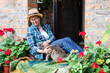 Happy woman and cat relaxing together on cozy home terrace in summer outdoors. Middle-aged farmer in backyard garden in blooming flowers. Inner peace, social rest, slow living, lifestyle moment