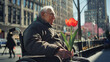An elderly man with Parkinson's disease and red tulip in his hands in wheelchair on city street