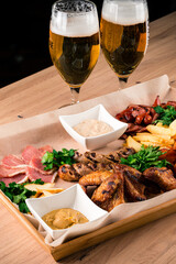 Canvas Print - Fried sausages with bacon, fried chicken wings, French fries, cheese, sauce and greens.