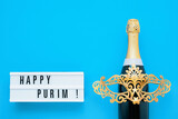 Fototapeta Tulipany - Purim background. Happy Purim written in lightbox, and champagne on a blue background. Copy space
