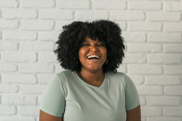 Canvas Print - Laughing African American woman with an afro hairstyle and good sense of humor smiling and laugh on brick wall at home background. Happiness and good emotions concept