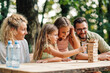 © Zamrznuti tonovi - Family is sitting at the table in nature and playing jenga game.