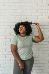 Canvas Print - Laughing African American woman with an afro hairstyle and good sense of humor smiling and laugh on brick wall at home background. Copy space. Happiness and good emotions concept