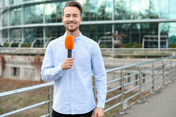 Canvas Print - Young male journalist with microphone working on city street