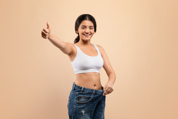 Wall Mural - Weight Loss Result. Indian Woman Wearing Oversized Jeans And Showing Thumb Up