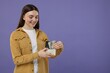 © New Africa - Happy woman putting dollar banknotes into wallet on purple background, space for text