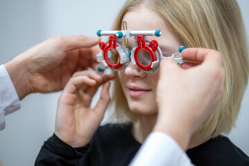 Wall Mural - portrait happy little girl patient ophthalmology clinic, vision test in progress cheerful child trying on trial frames during an optometric examination for accurate eyeglass fitting