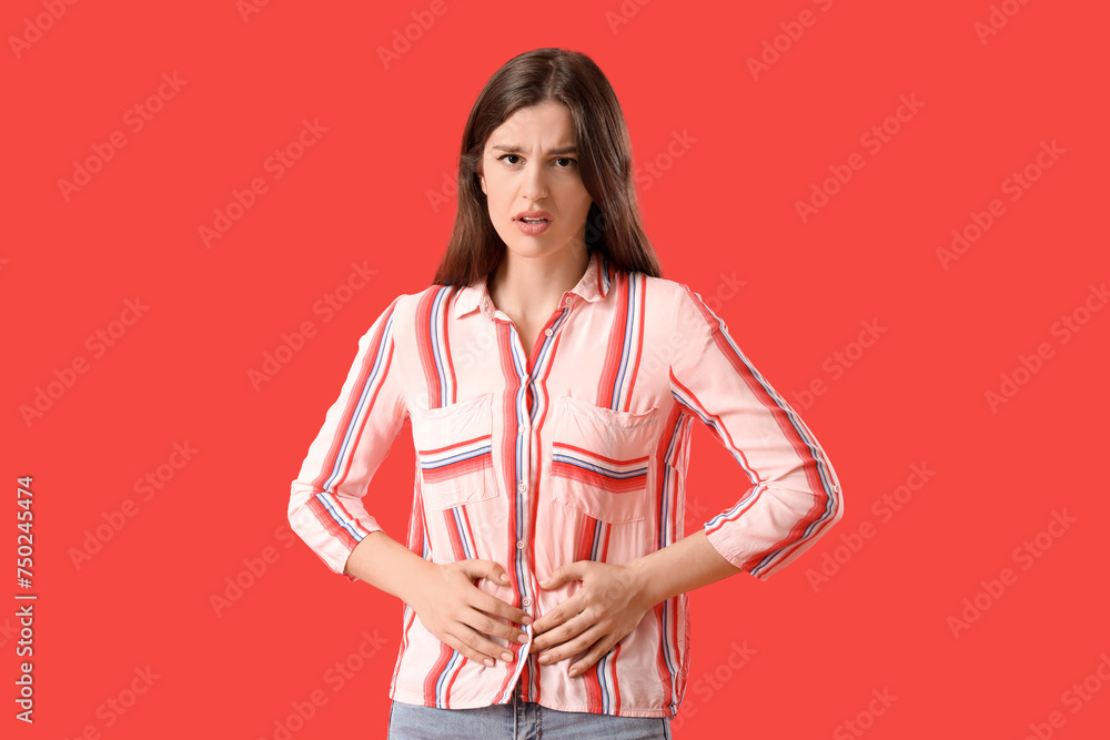Young woman suffering from stomach ache on red background