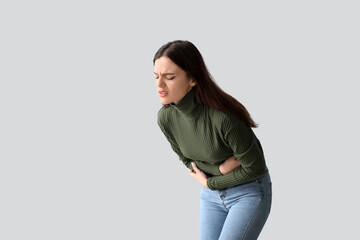 Wall Mural - Young woman suffering from stomach ache on light background