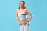 Fototapeta Panele - Upset young woman in tight jeans on blue background. Weight gain concept