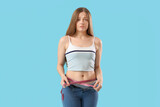 Fototapeta Panele - Upset young woman in tight jeans measuring her belly on blue background. Weight gain concept