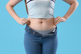 Fototapeta Panele - Young woman in tight jeans on blue background, closeup. Weight gain concept