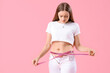 Young woman in tight pants measuring her belly on pink background. Weight gain concept