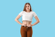 Upset young woman trying to button tight pants on blue background. Weight gain concept