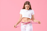 Fototapeta Panele - Young woman in tight pants measuring her belly on pink background. Weight gain concept