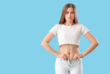 Fototapeta Panele - Upset young woman trying to button tight pants on blue background. Weight gain concept