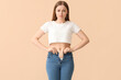 Sad young woman in tight jeans on beige background. Weight gain concept