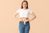 Fototapeta Panele - Sad young woman in tight jeans on beige background. Weight gain concept
