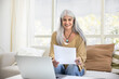© fizkes - Happy retired elderly Latin woman reading legal financial document at laptop, doing financial accounting paperwork, reviewing bills for online payment, holding paper letter, smiling, laughing