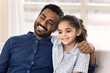 © fizkes - Happy loving young Indian dad and pretty preschool daughter kid looking away with toothy smiles, posing for home portrait. Positive father hugging cute child, enjoying fatherhood