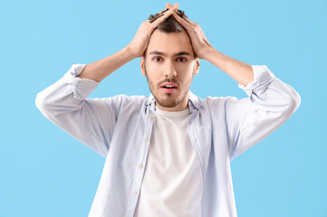 Shocked young brunette man with hair loss problem on blue background