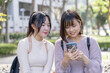 Two young Taiwanese female college students are sitting happily talking on the university campus in Taipei, Taiwan. 台湾台北の大学キャンパスで二人の若い台湾人女性の大学生が楽しそうに話しながら座っている