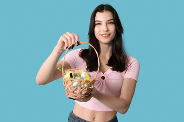 Canvas Print - Pretty young woman holding wicker Easter basket with cosmetics on blue background