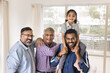 © fizkes - Happy young Indian dad holding little daughter kid on shoulders, standing near mature grandpa and great grand dad, looking at camera with toothy smile, posing for family generations portrait