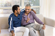 © fizkes - Happy older Indian father and positive young adult son talking on home sofa, hugging, having fun, laughing at jokes, enjoying conversation, discussion, friendship, family meeting