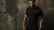 Muscular tattooed man in a black t-shirt posing against a textured grey wall.