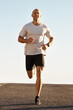 © Katie/peopleimages.com - Man, running in street and fitness for cardio, health and fresh air when training for marathon with sky background. Sports, exercise and athlete in portrait for workout, wellness and endurance