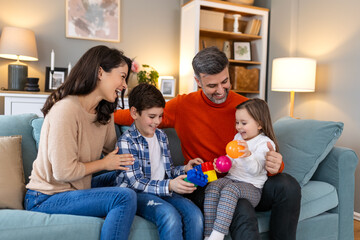 Wall Mural - Cheerful son and daughter sitting with parents playing at home. Playful little boy and girl enjoying spending time with parents at home.