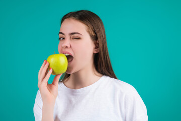 Young woman bitting apple, healthy lifestyle. Girls holds a fresh green apple studio portrait on green isolated background. Healthy food. Fruit for healthy teeth. Woman holding apple.