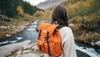 Cheerful female  carries touristic rucksack, has camping expedition, stands near mountain stream, breathes fresh air