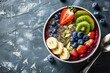 Healthy summer acai smoothie bowl with chia seeds, fresh banana, strawberry, blueberry, cocos, kiwi top view on rustic concrete background with spoon 