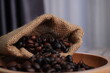 close up of coffee beans in a sack pouring into wooden bowl