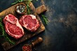 Two raw uncooked meat beef rib eye marbled steaks on wooden cutting board with seasonings on dark rustic background ready to be grilled from above, preparing dinner with meat, space for text 