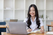 © SOMKID - Happy young asian woman wearing earphones and using laptop computer at desk in office, Female asian student with laptop computer, College female student learning online.