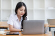 © SOMKID - Happy young asian woman wearing earphones and using laptop computer at desk in office, Female asian student with laptop computer, College female student learning online.