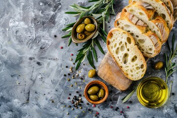 Wall Mural - Slices of fresh ciabatta, green and brown olives, olive oil with rosemary, olive tree branches on gray concrete stone rustic background overhead