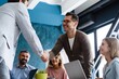 © opolja - Welcome on board. Confident men shaking hands and smiling while sitting at the desk in office