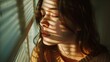 Young woman with shadow stripes on her face from window blinds. Intimate indoor portrait with natural light. Contemplation and personal space concept. Design for introspection, mental health