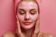 Close up photo of woman applying cosmetic face mask on her face. Young beautiful woman in towel on pink background and copy space for text, cosmetology spa concept