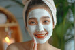 Woman applying facial clay mask. Smiling asian girl in towel with cosmetic peel off mask on her face. Beauty and spa treatment. Natural skin care and cleansing concept