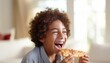 Happy young boy enjoying tasty pizza in defocused kitchen background with space for text