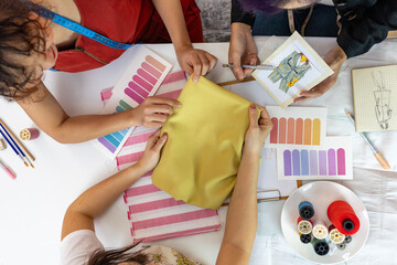 Wall Mural - Team of fashionable freelance dressmakers and customer choosing design and fabric color for new custom dress while working in artistic workshop studio for fashion design and clothing business industry