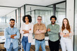 © Vadim Pastuh - A vibrant team of five professionals stands with confidence in office, arms crossed and smiles wide, representing the epitome of a diverse and dynamic workgroup poised for collaboration and success