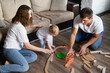 © GRON777 - Parents play with a toddler, sit on the floor and build a wooden railroad. Concept family weekend at home, educational toys. Caring parents enjoying educational activities with their child