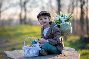 Beautiful stylish toddler child, boy, playing with Easter decoration in the park, springtime