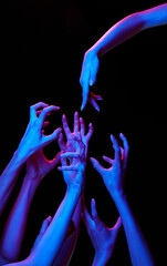 One pointing hand diving to group of hand showcasing negative in multicolored neon lighting against black studio background. Concept of human touch, beauty and care, spa procedures.